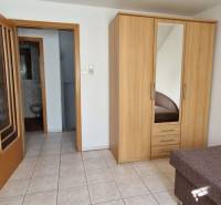 A room in a family house with a bed, wardrobe, shelves, and a bathroom.