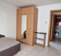 A room in a family house with a bed, a wardrobe, and a view into the bathroom with a washing machine.