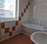 A bathroom with a bathtub and sinks in a family house, with tiles and a window.