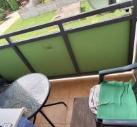 A balcony of a 3-room apartment with a plastic chair and a small glass table.