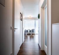 A hallway leading to the living room in a two-room apartment, with wooden flooring and white walls.