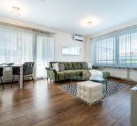 Living room in a two-room apartment with wooden flooring, a sofa, and a dining table.