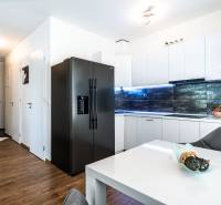 A kitchen in a 2-room apartment with white cabinets, a black refrigerator, and wooden flooring.