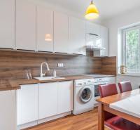 A kitchen with a large window, dining table, washing machine, and wooden paneling in a 2-room apartment.