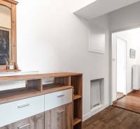 A dresser with a wooden mirror in the hallway of a two-room apartment, leading to a bright corridor.