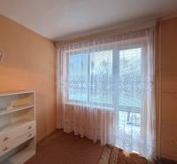 A room in a three-room apartment with orange walls and a white curtain on the window.
