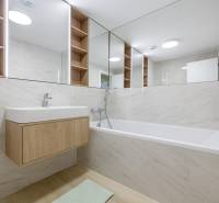 Bathroom with a bathtub, sink, and wooden shelves in a 3-room apartment.