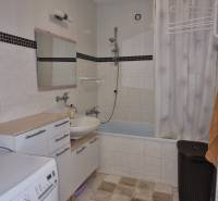 A bathroom in a 4-room apartment with a bathtub, sink, washing machine, and storage cabinets.
