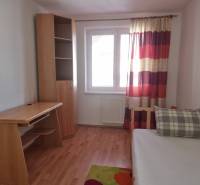 A room in a 4-room apartment with a wooden table, a wardrobe, and a bed with a pillow.