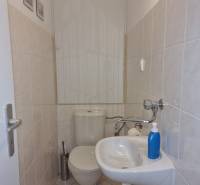A small bathroom in a 4-room apartment with a toilet, sink, and light-colored tiles.