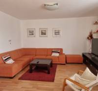 Living room of a 4-room apartment with an orange sofa, TV, and decorations on the shelves.