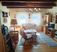 A cottage with a wooden ceiling, a sofa set, a guitar, shelves, and decorative items.