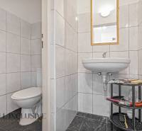 Bathroom in commercial premises with a sink, toilet, and shelf for accessories.