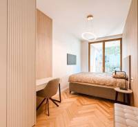 A bedroom with a desk and a chair in a four-room apartment, with a large window and wooden flooring.