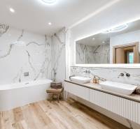 A bathroom with a bathtub and double sink in a 4-room apartment, marble walls and wooden floor.