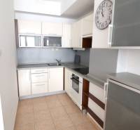 A kitchen in a 2-room apartment with tiles, appliances, and a wall clock.