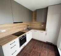 A kitchen in a 2-room apartment with wooden cabinets and dark tiles.