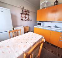 A kitchen in a 2-room apartment with an orange kitchen unit, a white refrigerator, and a dining table.