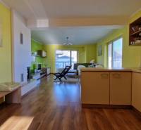 Interior of a holiday apartment with wooden flooring, an armchair, and a kitchen unit in warm colors.