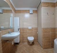 Bathroom in a holiday apartment with a sink, mirror, and toilet, tiled with brown tiles.