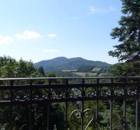 The view from the cottage of the mountain range in Štiavnické Bane, framed by metal railings and trees.