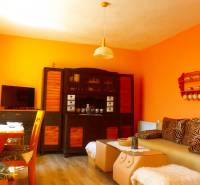 A living space in a cottage with orange walls, a sofa, and a television.