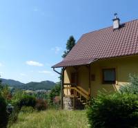 A cottage in Štiavnické Bane, surrounded by greenery and with a view of the hills in the background.