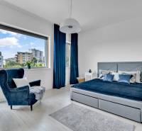 A bright bedroom in a 4-room apartment with a large window, blue curtains, and a comfortable chair.