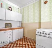 A kitchen with white cabinets, a stove, and patterned green wallpaper in a family house.