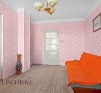 A room in a family house with an orange sofa, pink wallpaper, and a vase on a wooden floor.