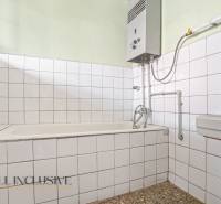 A bathroom in a family house with white tiles and a gas water heater.