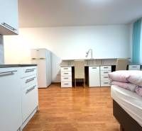 A studio apartment with a bright interior, a kitchenette, a table, two chairs, and a bed.