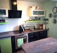 A kitchen in a family house with appliances, hanging plates, and cabinets with shelves.