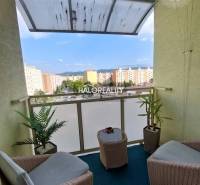 A balcony of a 3-room apartment with rattan furniture and a view of the housing estate in Prievidza.