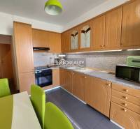 A kitchen in a 3-room apartment with a wooden cabinet and green chairs.