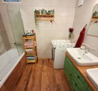 A bathroom in a 4-room apartment with a bathtub, sink, and washing machine on a wooden floor.