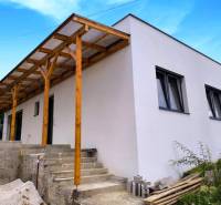 A family house in Malé Kršteňany with a wooden extension and concrete stairs, blue sky.