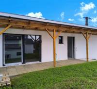 A family house in Malé Kršteňany with a wooden pergola and lawn on a sunny day.
