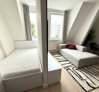 A studio apartment with a light bed, a gray sofa, and a black and white carpet.