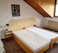 A double bed under a slanted ceiling in a 2-room apartment with a painting on the wall.