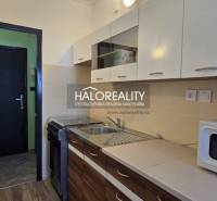 A kitchen in a studio apartment with white and wooden cabinets, a microwave, and a dining counter.