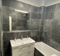 A bathroom with gray tiles and white sanitary ware in a 4-room apartment.