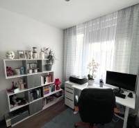 A study in a four-room apartment with shelves, a table, a chair, and a window with curtains.