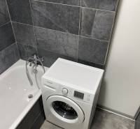 A bathroom in a 4-room apartment with a bathtub and a washing machine in dark gray tiles.