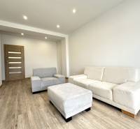 A bright living room in a two-room apartment with beige furniture and wooden flooring.