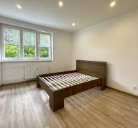 Bright bedroom with a wooden bed in a 2-room apartment with large windows.