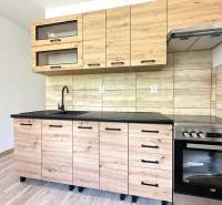A kitchen with wooden paneling in a 2-room apartment, equipped with glass cabinets and a stove.