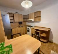 A kitchen in a one-room apartment equipped with wooden furniture and a refrigerator.