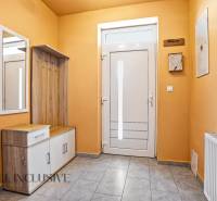 A hallway in a family house with a shoe cabinet, coat racks, a mirror, and white doors.