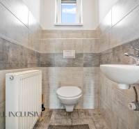 Bathroom in a family house with a toilet, sink, and radiator; light tiles.